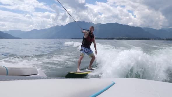 Guy wakeboarding on splashing waves generated by the boat which pulls him