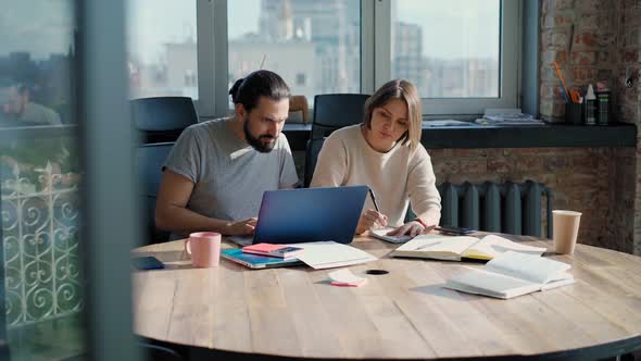 Two Coworkers are Discussing a Project While Sitting in Front of Their Laptops