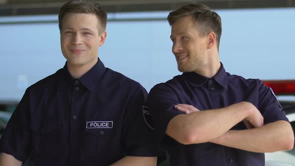 Friendly Police Officers Crossing Hands and Smiling Into Camera Against Car