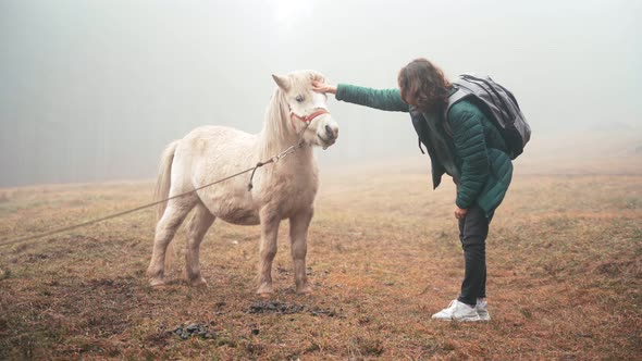 A Young Woman Strokes a White Pony Outdoors on a Foggy Fall Day