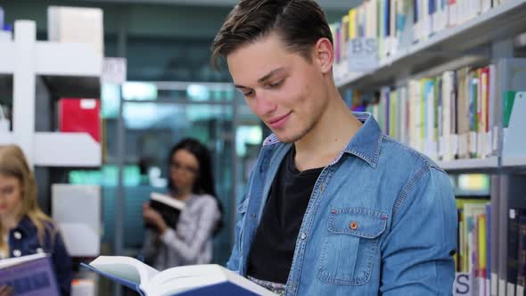 Library. Smiling Male Student Reading Book Near Shelves
