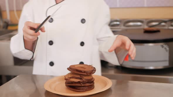 Child Boy in Chef's Costume Prepares Chocolate Pancakes in Kitchen in Cafe