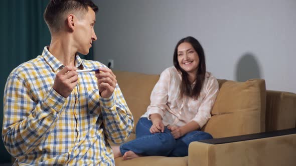 Young Man with a Pregnancy Test Looks Back at the Happy Woman