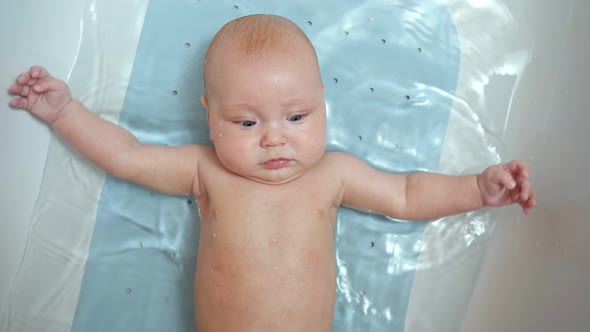 Baby Girl Lies in Bath Water and Looks Directly at Parents