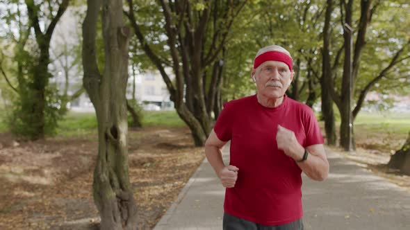 Male Senior Person Running Along the Road in Park. Mature Runner Man Training, Listening Music