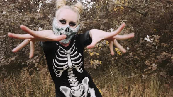 A girl with a scary make-up in a skeleton costume, a mask with rhinestones in a gloomy autumn forest