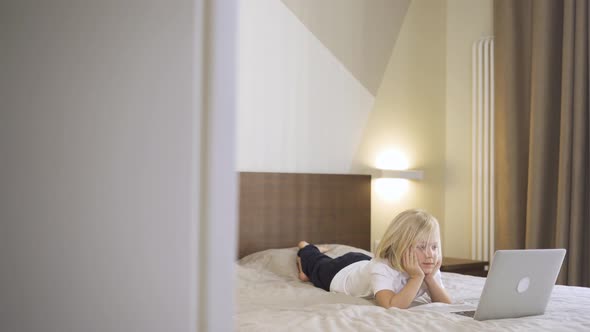 a Cute Preschool Boy Lying on the Bed and Watching a Video on a Laptop. Distance Learning Online