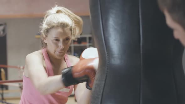 Confident Blond Caucasian Woman Boxing Punching Bag in Sports Club. Portrait of Concentrated Female