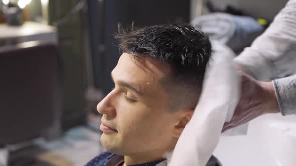 Hairdresser Wipes Hair of Brunette Man with Disposable Towel After Washing Hair