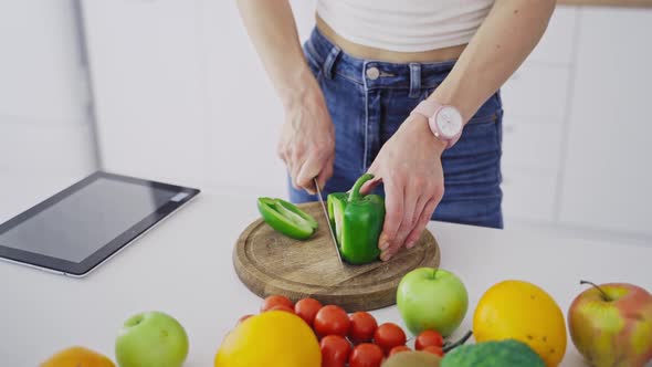 Young female is cutting green pepper on a wooden board.