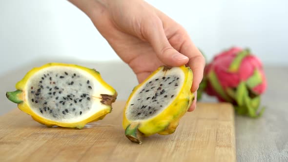 Female Hands is Cutting a Dragon Fruit or Pitaya with Yellow Skin and White Pulp with Black Seeds on