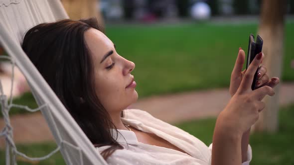 Close Up of a Woman Laying in a Hammock Outdoors Surfing Internet on Tablet Clicks on the Screen