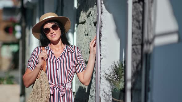 Smiling Young Woman in Straw Hat and Sunglasses Posing at City Street