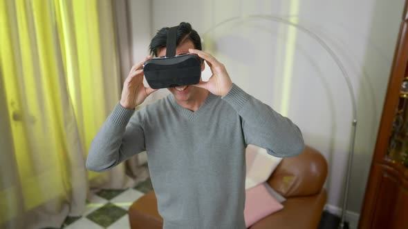 Happy Smiling Middle Eastern Man in VR Headset Standing in Living Room at Home