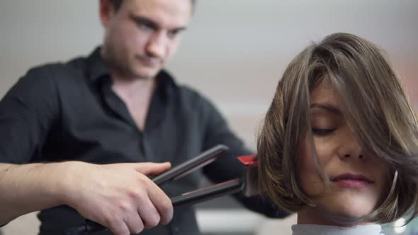 Hair Stylist Makes Professional Hairstyle of Young Woman in Beauty Studio