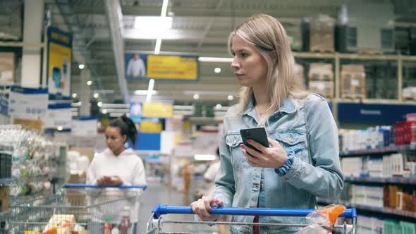 A Woman is Browsing Her Phone While Shopping in the Supermarket