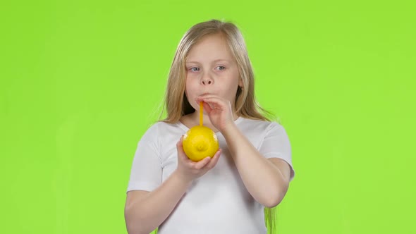 Little Girl Is Holding a Lemon and Drinking Juice From a Lemon Through a Straw. Green Screen