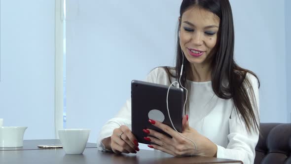 Smiling Woman in Earphones Having Video Call Via Digital Tablet in a Cafe