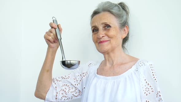 Emotional Senior Woman with Silver Hair is Holding Metal Ladle or Scoop on White Background Happy