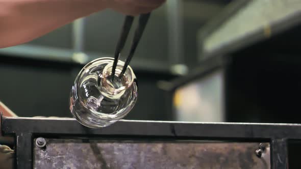 Low angle close up of glass artist spinning a vase, shaping the opening.