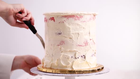 Baker frosting pink and purple cake with a white buttercream icing.