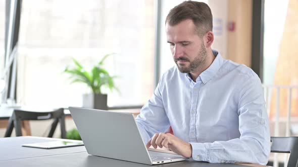 Young Man with Laptop Looking at Camera in Office 