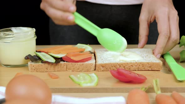 Woman's hands spreading salad cream on whole wheat bread for making healthy sandwich