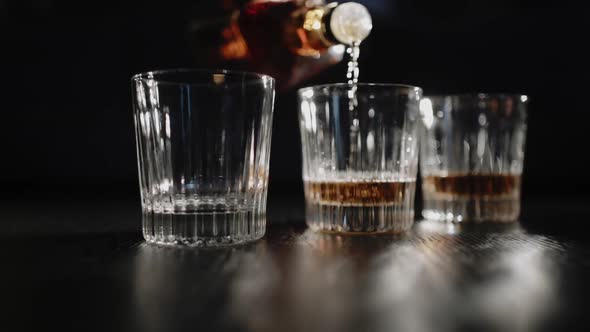 Bartender pours alcohol drink in whisky glasses