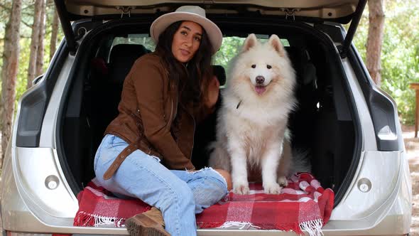A woman hugs and strokes a dog in the trunk outdoors in the forest. Traveling with animals.