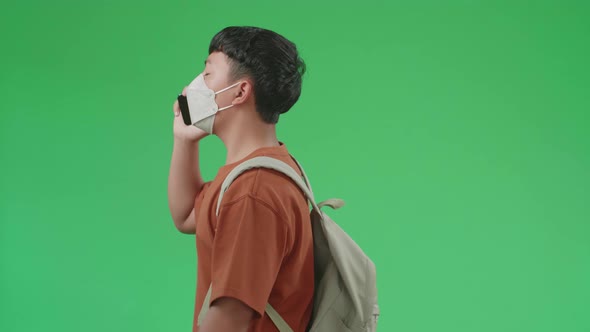 The Side View Of Asian Boy Student Talking On Mobile Phone While Walking On Green Screen