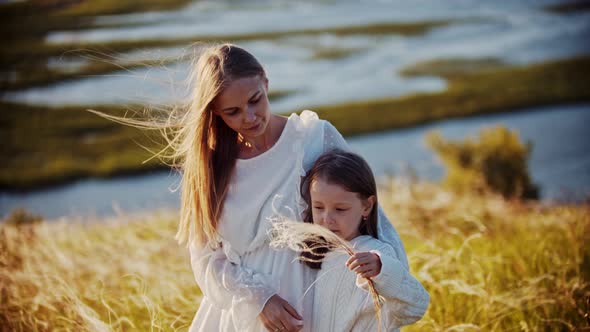 Young Smiling Woman Hugging Her Daughter Standing on the Wheat Field - Girl Waving Her Hand with the