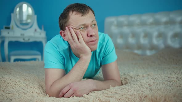 Portrait of a man in the bedroom on the bed lies thinking
