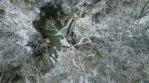 Waterfall Flowing Down From Rocks Shot Through the Branches of a Tree in Winter