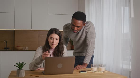 Young Couple are Discussing Something in Front of a Laptop in Their Kitchen at Home