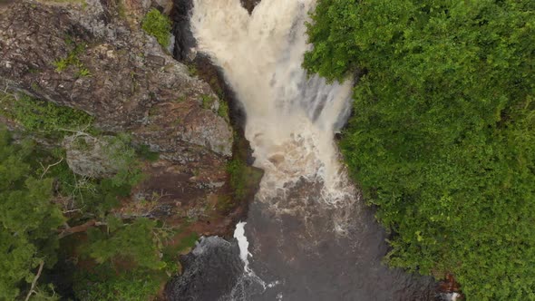 Birds eye view aerial shot of a river cascading over the edge of a cliff into a waterfall in the jun