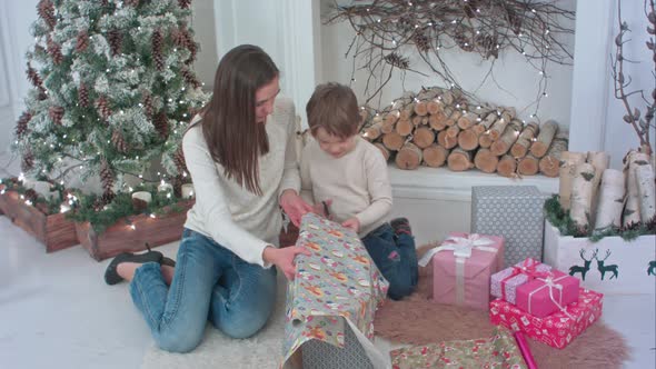 Cute Little Boy Helping His Mother To Cut Paper for Wrapping Up Christmas Presents