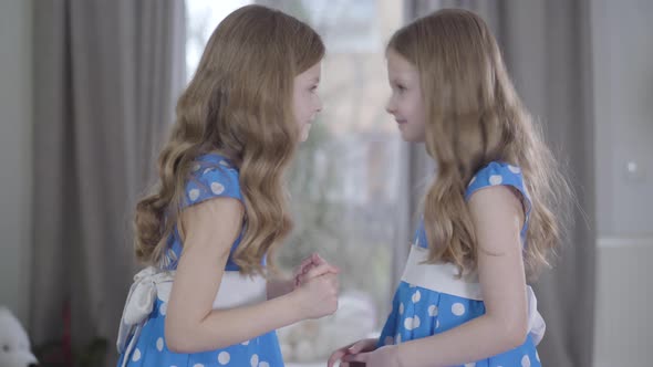 Side View of Happy Smiling Caucasian Girls in Blue Dresses Sharing Secrets and Giving High Five