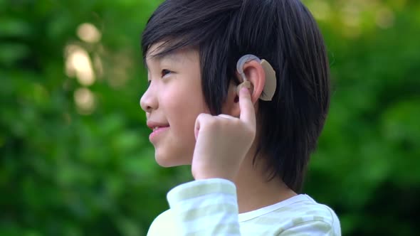 Asian Child With Hearing Aid Behind The Ear Outdoors