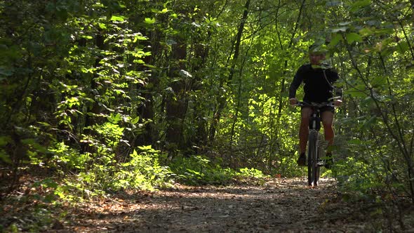 A Cyclist Rides Down a Path Through a Forest - Front View