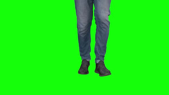 Man Runs at the Green Screen. Close Up. View From the Bottom. Guy in Jeans and Sneakers.