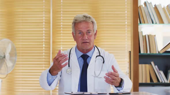 Portrait of male caucasian doctor of talking looking at camera while sitting in hospital