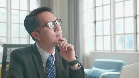 Asian Businessman Thinking While Using Computer For Working At Home