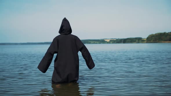 Scary figure in black mantle in the river. Mysticism of Halloween. Halloween costume.