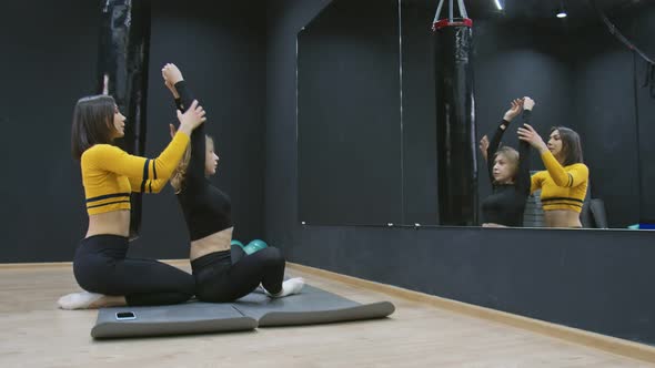 Female Trainer in Yellow Sportswear is Stretching Young Woman in Black Sportswear