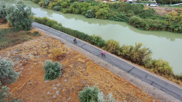 Couple riding bicycles along a trail by a river together - aerial tracking view