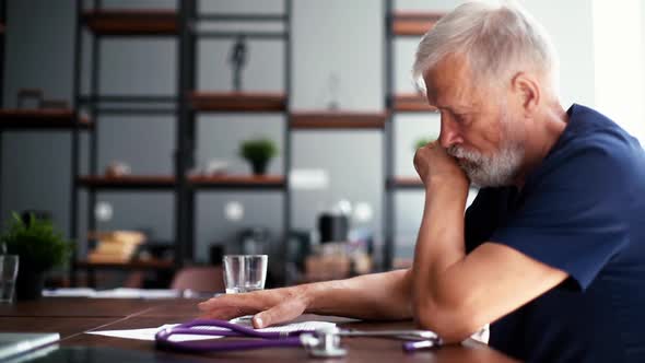 Focused Thoughtful Gray-haired Mature Man Doctor Studying Medical Report of Patient Sitting at Desk.