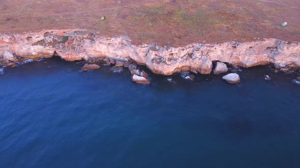 Top down aerial view of waves splash against rocky seashore, background. Flight over high cliffs of