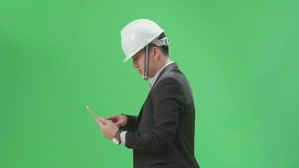 Side View Of Asian Chief Engineer In The Hard Hat Use Tablet While Walking On Green Screen