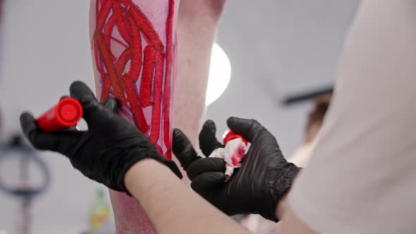 Tattoo Artist Drawing a Sketch with Letters on the Leg on His Client