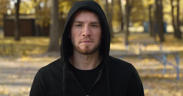 Young Caucasian Man Wearing Hoodie Raising Head and Looking Seriously to Camera Posing Outdoors in